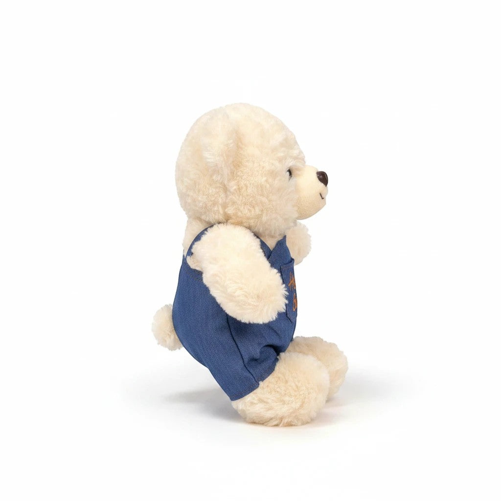 دب محشو ناعم من TagerlSaada بلون كريمي يرتدي وزرة جينز زرقاء مطرزة بعبارة Hello Bear، مثالي للعناق واللعب.