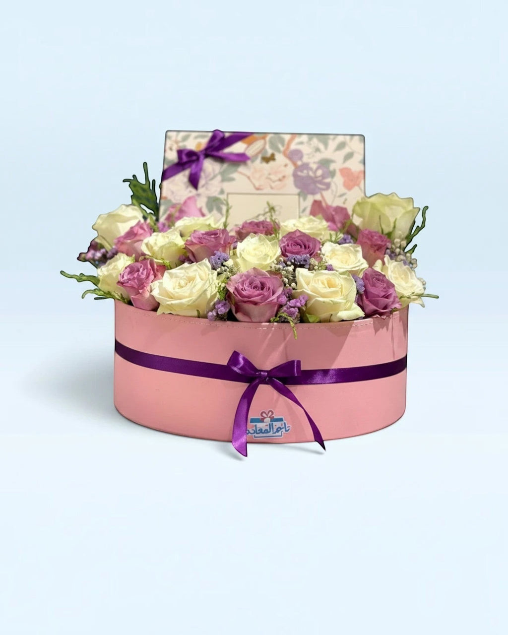 تنسيق زهور طبيعية بيضاء وأرجوانية فاخرة في صندوق هدايا دائري وردي من TagerlSaada مع شريط أرجواني أنيق